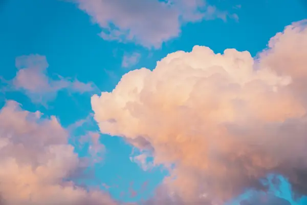 Large peach and white cumulus clouds illuminated by warm sunset light against a vivid blue sky.